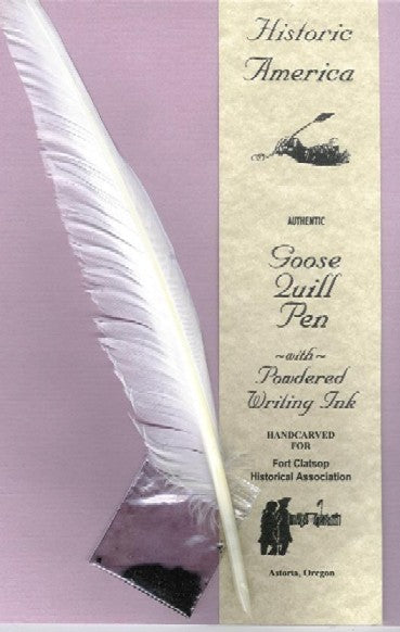 A goose quill with a sharpened point for writing alongside a pouch of dry ink powder. A label saying "Historic America. Authentic Goose Quill Pen with Powdered Writing Ink. Hand carved for Fort Clatsop Historical Association" is beside it.