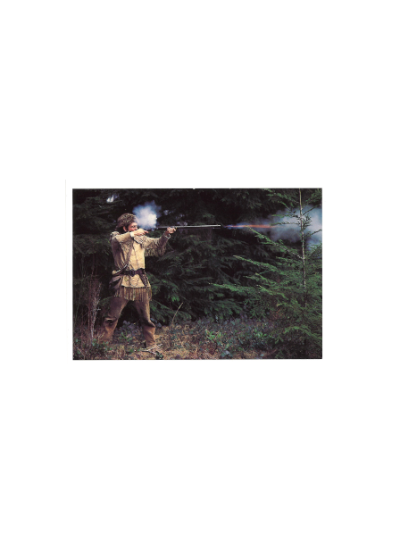 A park ranger in historical costuming fires a flintlock musket into the woods with smoke and flame coming off the barrel.