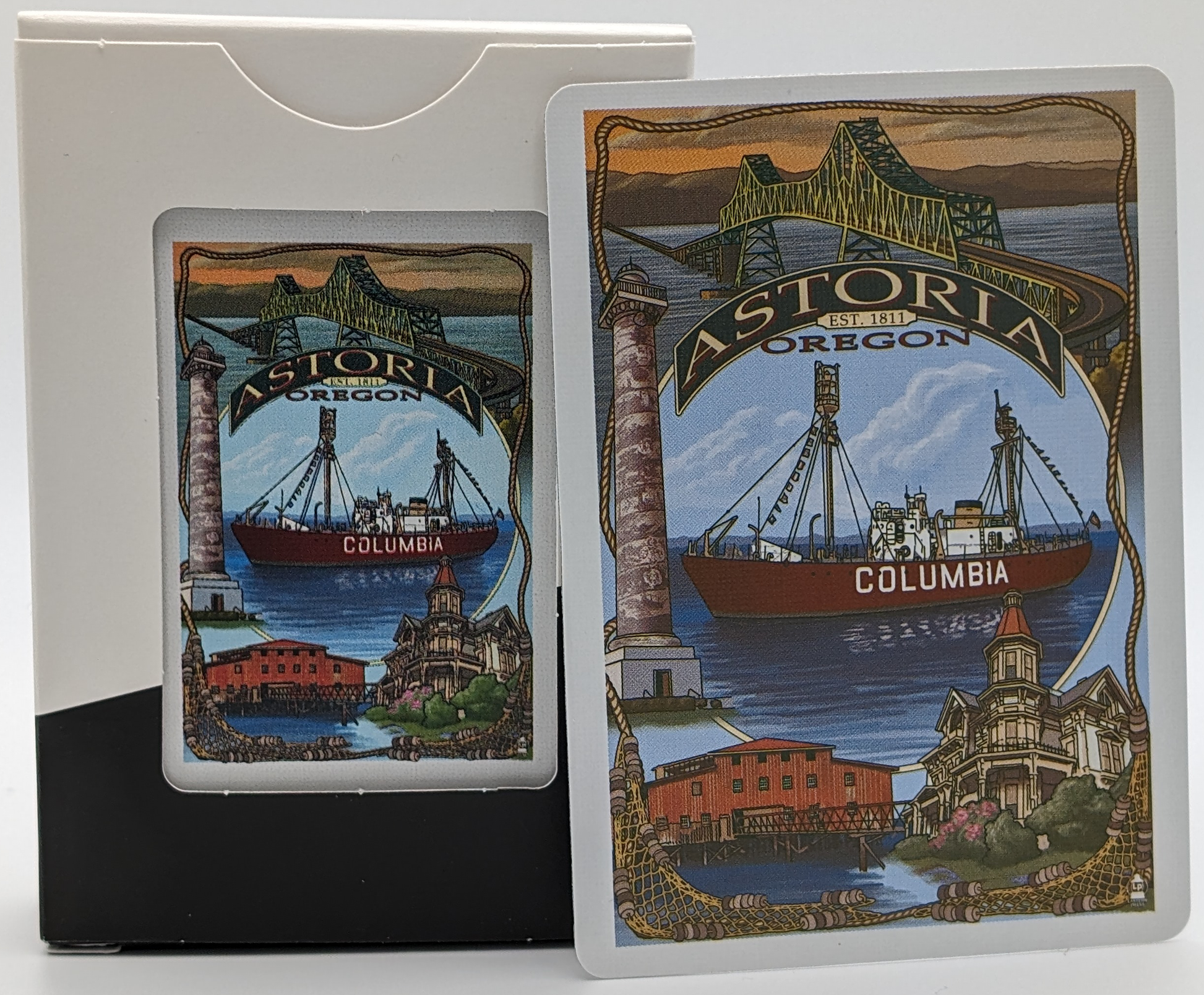 The back of a deck of themed playing cards featuring art depicting the Astoria Megler Bridge, the Light Ship Columbia, the Astoria Column, The Flavell House, and a red building on a pier.