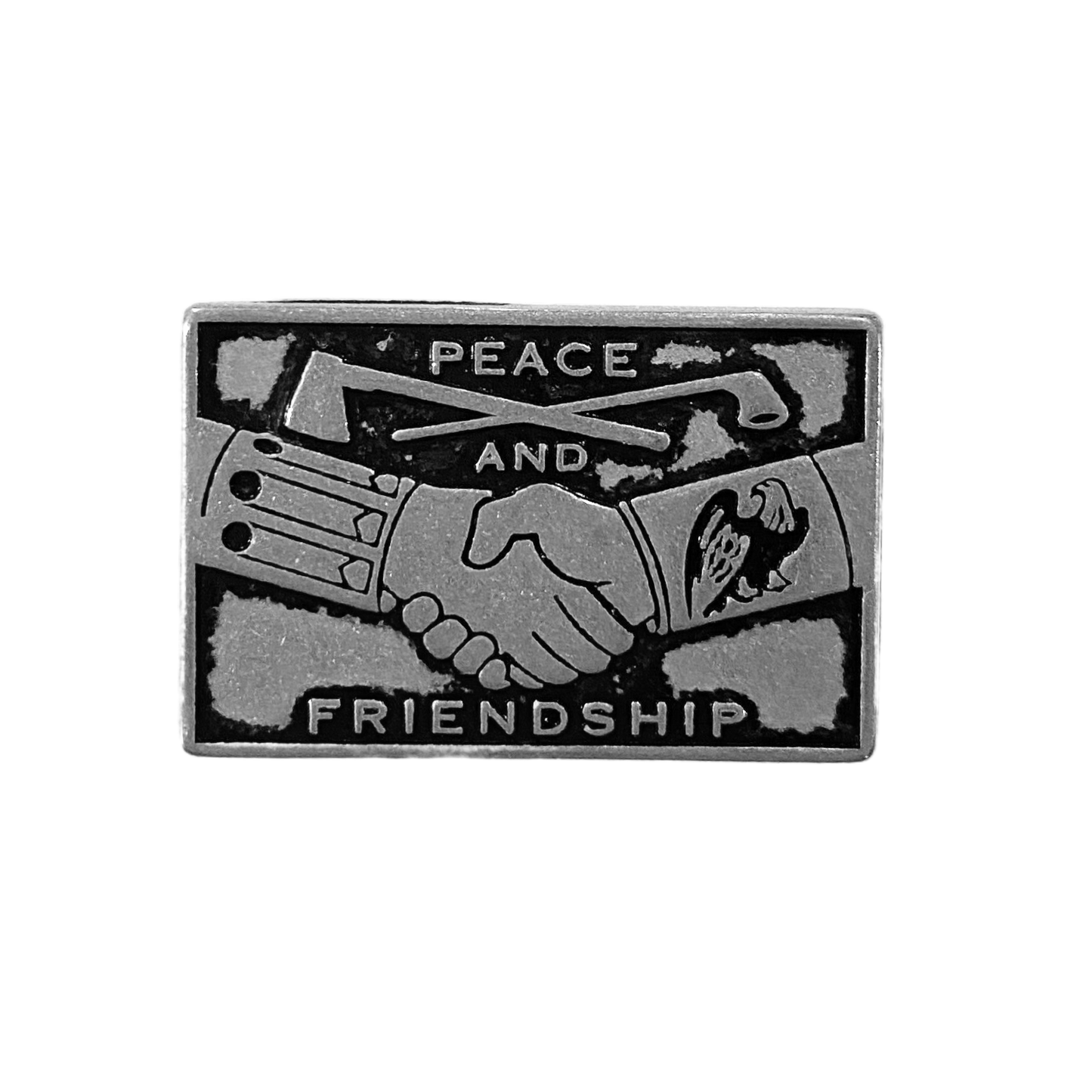A small rectangular token with a depiction of shaking hands underneath a tomahawk and pipe reading "Peace and Friendship"