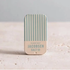 An upright small tin of sea salt, the label reading "Jacobsen Salt co" with a blue and white pinwheel stripe design.