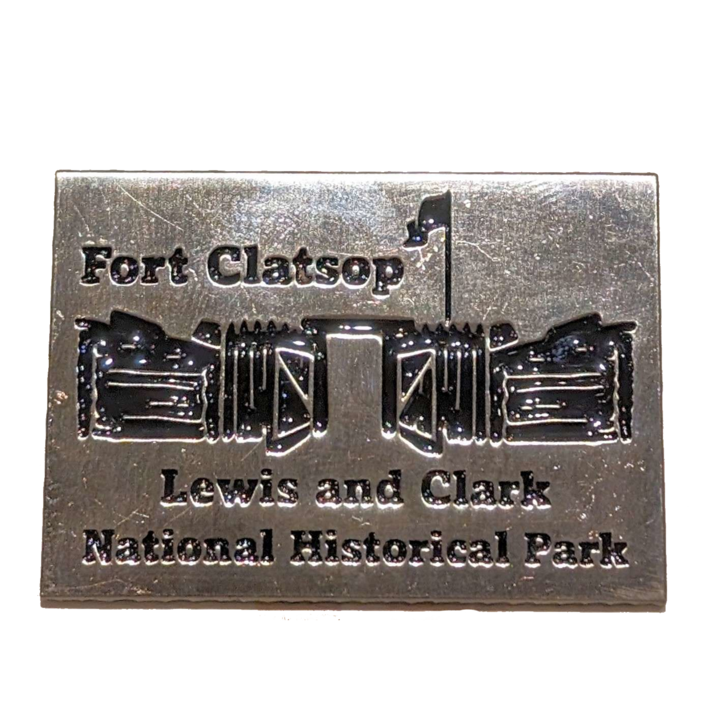 A rectangular metal pin with the text "Fort Clatsop Lewis and Clark National Historical Park" and an a depiction of Fort Clatsop.